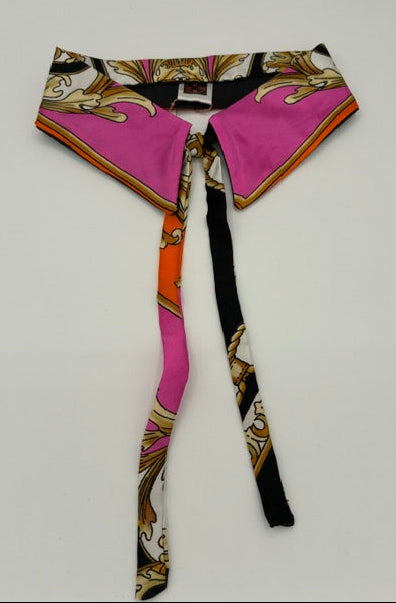 A silk collar with a vibrant magenta pink, black, gold, and white baroque pattern, laid flat on a light gray back