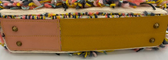 A rectangular handbag with a multicolor fringed top and bottom, featuring a split-tone back panel with a pink leather section on the left and a mustard yellow leather section on the right, secured with brass grommets.