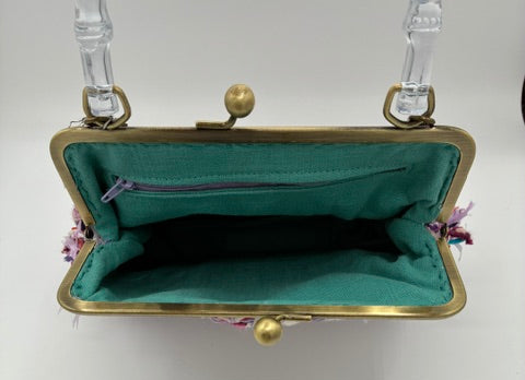 An open vintage kiss-lock handbag with a teal green velvet interior, gold-tone metal frame, and clear plastic shoulder straps, shown against a plain white background.