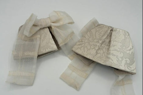 A pair of cream-colored woven fabric headbands with a subtle damask pattern and striped trim, laid out on a plain white surface.