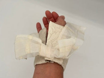 A close-up of a person's hand and wrist wrapped in a beige fabric wrist wrap or splint, photographed against a white studio backdrop with softbox edges visible.
