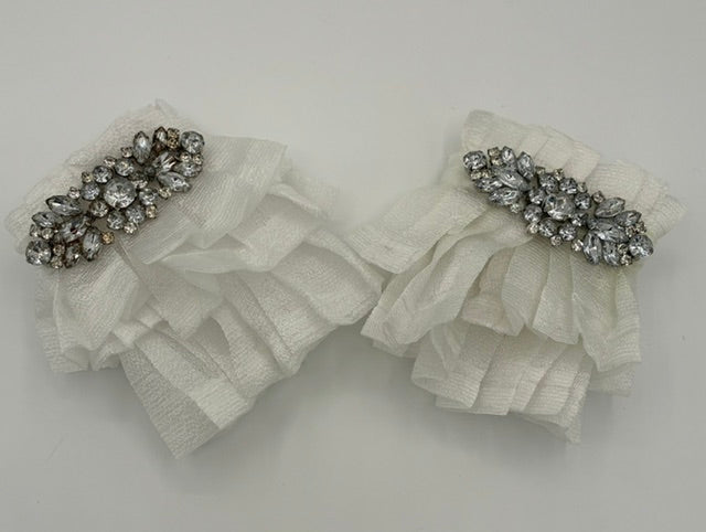A pair of white pleated fabric hair cuffs decorated with silver-toned crystal embellishments, displayed on a light gray background.