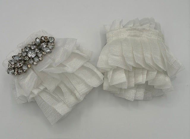 A pair of white pleated  organza wrist cuffs  with a silver rhinestone embellishment on one clip, displayed on a light gray background.