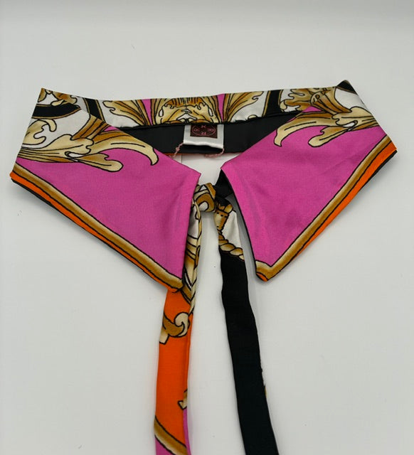 A silk scarf collar with a vibrant pink, orange, black, and gold baroque pattern, laid flat on a white background.