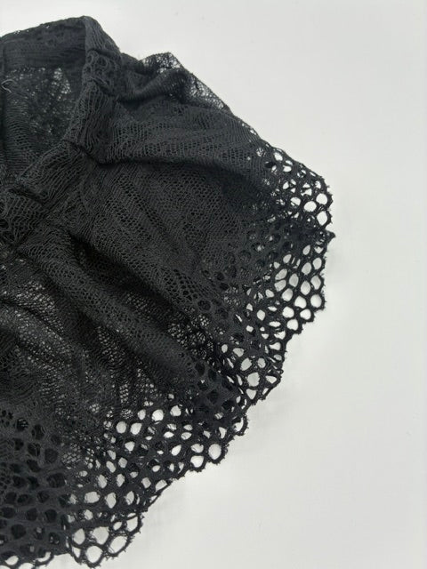 Black lace fabric with an intricate openwork pattern, draped against a plain light gray background.