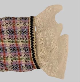 A close-up of a tweed fabric sleeve or cuff in a multicolor plaid pattern with a white lace trim and a black decorative edge, set against a plain beige background.