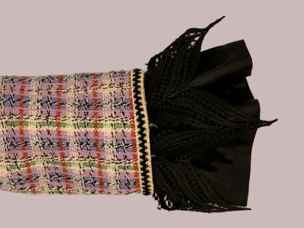 A close-up of a tweed sleeve with a multicolor plaid pattern and a black lace cuff,