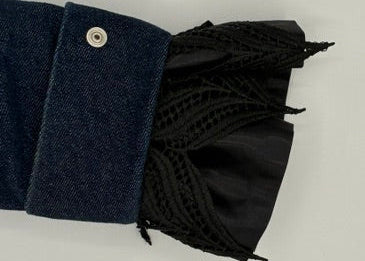A close-up of a dark blue denim sleeve with a single silver snap button and a black lace and satin cuff 