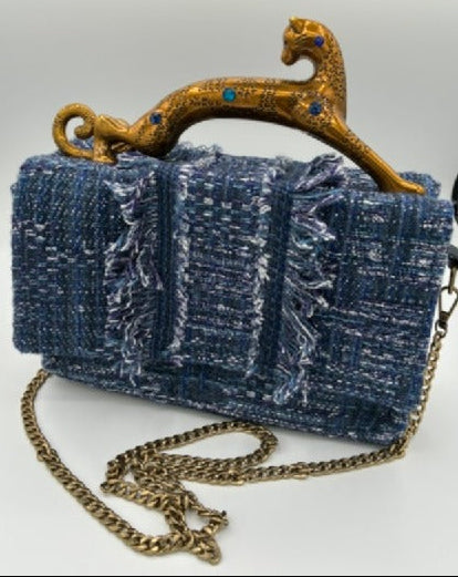 A blue tweed clutch purse with a gold leopard-shaped handle and a gold chain strap, set against a light gray background.