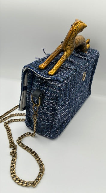 A small structured handbag with leopard handlein blue and white tweed with a gold-tone chain strap and a decorative gold-tone handle, photographed against a plain light background.