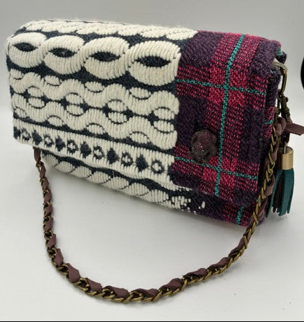 A small woven shoulder bag with a dark purple and red plaid top section, a cream and black geometric patterned body, and a brown leather chain strap on a plain white background.