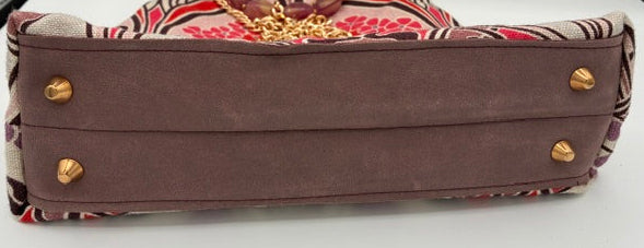 A vintage-style handbag shown from the back, featuring a dark brown suede-like panel with gold-tone rivets, a patterned fabric body in red, beige, and black, and a gold chain handle.