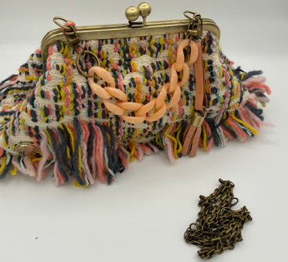 A multicolor tweed fringed clutch purse with a gold-tone kiss-lock clasp and a chunky peach chain strap, displayed on a white background with a small gold chain accessory nearby.