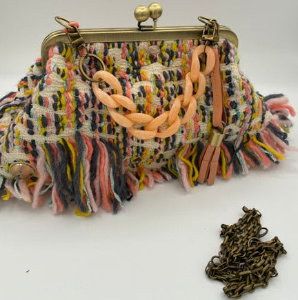 A multicolor fringed tweed handbag with a gold-tone kiss-lock clasp and a chunky peach chain strap, shown on a white background with its matching chain accessory placed nearby.