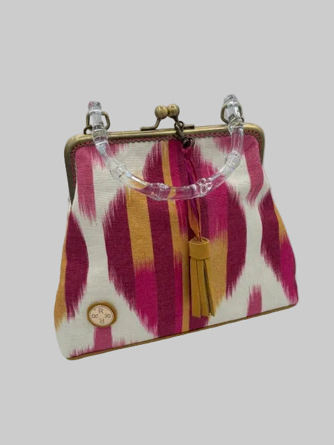 A small clutch purse with a pink, gold, and white ikat pattern, featuring a clear acrylic handle, gold-tone metal clasp, and a tan leather tassel.
