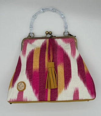 A small handbag with a pink, white, and yellow ikat pattern, featuring a clear bamboo style  bamboo handle and a gold-tone tassel clasp, photographed on a white background.