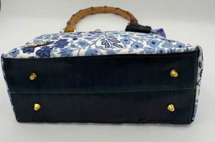A small handbag with a navy blue leather base, a blue and white floral patterned top, a bamboo handle, and gold-tone hardware, shown on a white surface.
