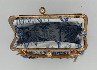 A small vintage-style handbag  with a blue and white toile patterned fabric lining and a gold-tone metal frame, shown against a plain light gray background.