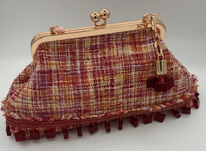 A tweed clutch bag with a gold-tone kiss-lock frame, featuring a textured plaid pattern in red, yellow, orange, pink with a bead fringe edge and a small hanging charm.