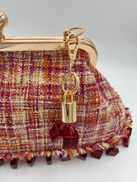 Close-up of a tweed clutch purse featuring a multicolor woven pattern of red, orange, and beige, with a gold-tone metal frame and a decorative dark red beaded fringe.