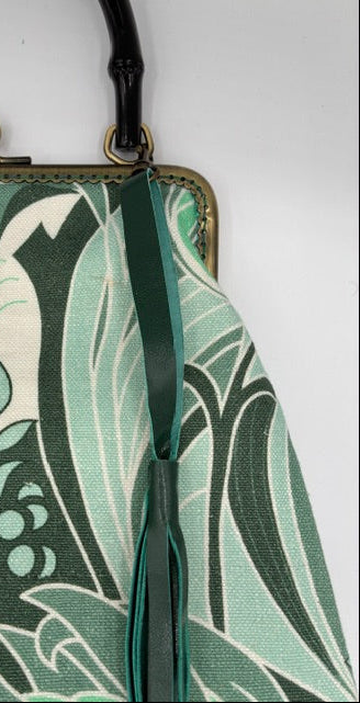 Close-up of a vintage Art Deco patterned handbag in green, white, and teal tones, featuring a dark green leather strap and antique brass clasp.