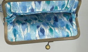 A hand holding an open vintage-style kiss-lock handbag with a blue and white patterned fabric lining and a dark brown handle, shown against a plain white background.