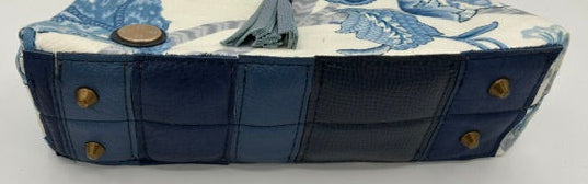 A structured handbag with a blue and white floral toile pattern on the top, dark blue quilted sides, brass-tone studs, and a dark brown leather top handle, shown on a plain white surface.
