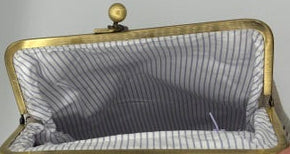 A hand holding an open vintage-style kiss-lock handbag with a striped lining, black handle, and gold-tone metal frame.