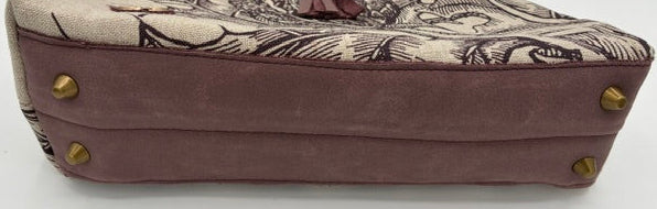 A structured handbag with a dusty mauve suede lower half and a beige canvas upper half featuring a dark brown sketch-style illustration. It has a matching mauve leather tassel pull and a black top handle, accented with brass studs on the sides.