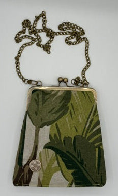A small crossbody bag with a green tropical leaf print, featuring an antique bronze metal frame and a matching chain strap, displayed on a plain white surface.