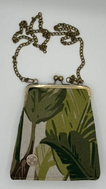 A small crossbody bag with a green tropical leaf print, featuring an antique bronze metal frame and a matching chain strap, displayed on a plain white surface.