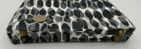 A small handbag with a black and white spotted animal print pattern, featuring gold-tone hardware and a chain strap, resting on a white surface.