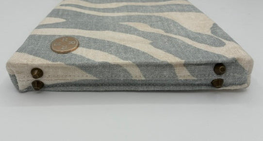 A fabric small crossbody stadium sized purse with a light blue  and cream zebra stripe pattern, featuring a brass-tone metal clasp closure at the top and decorative brass-tone snap buttons on the sides.