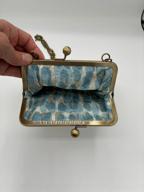 A small  kiss lock  case with a brass frame and a blue and white patterned fabric lining, held open by a hand against a plain white background.