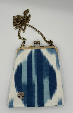 A small crossbody stadium ready  purse with a blue and white ikat pattern, featuring a gold-tone metal frame and a matching chain strap with a decorative clasp.