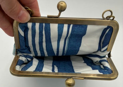 A vintage-style kiss-lock clutch purse with a blue and white striped fabric lining and a brass frame, held open by a hand against a plain white background.