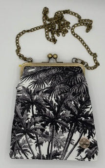 A small crossbody kisslock purse with a black and white palm tree pattern, featuring an antique bronze-tone metal chain strap and clasp, resting on a plain white surface.