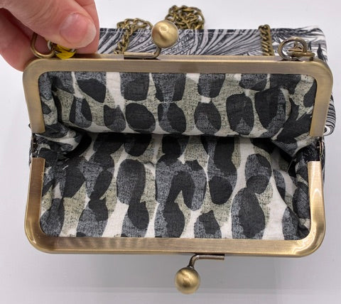 A small kiss-lock clutch bag with a black and white patterned fabric exterior and a matching patterned fabric lining, held open by a hand against a plain white background.
