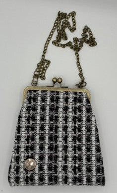 A small crossbody tweed kiss-lock handbag with a black and white houndstooth pattern, antique bronze chain strap, and a decorative pearl accent on the front