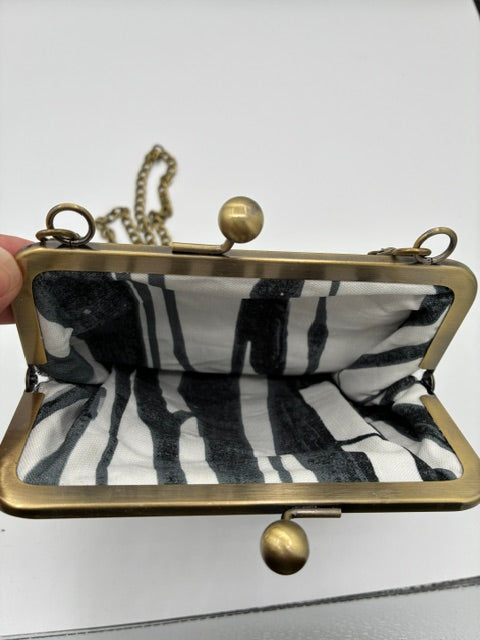 A small crossbody kiss-lock purse with a black and white tweed fabric lining and an antique brass frame, held open by a hand against a white background.
