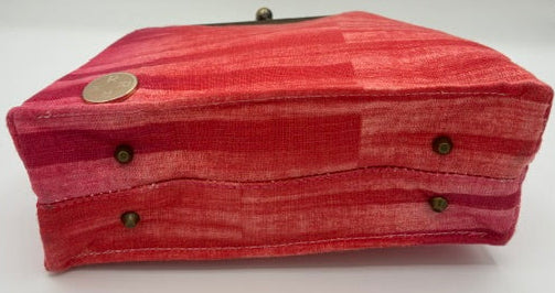 A rectangular fabric-covered case or box with a textured red and pink striped pattern, featuring brass-tone metal snaps and a clasp, photographed on a white studio background.