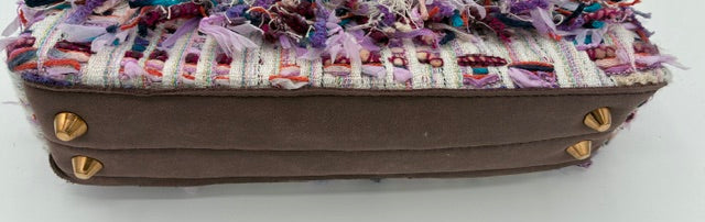 A small structured handbag with a brown suede-like base, a multicolor woven tweed top, and frayed tulle embellishments across the front. The bag has gold-tone studs and a clear plastic handle on a white background.