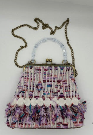 A small tweed handbag with a multicolor pattern of pink, purple, and white threads, featuring a clear plastic handle, antique bronze frame, and a fringed tassel detail along the bottom. It is shown with a matching chain strap on a plain white background.