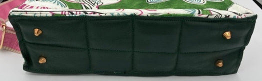 A handbag shown from the bottom side, featuring a dark green quilted base with gold-tone metal studs and a top flap in a green, white, and pink paisley pattern.