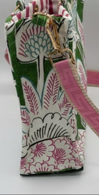 A tote bag with a pink strap, featuring a green, white, and pink botanical block-print pattern, gold-tone metal hardware, and a bamboo-style clasp, shown on a plain white background.
