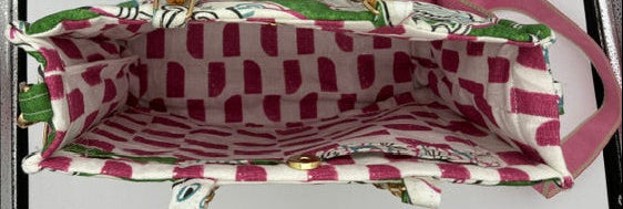 An open fabric tote bag shown from the inside, featuring a pink and white patterned lining with green accents and a pink shoulder strap, photographed against a light gray background.