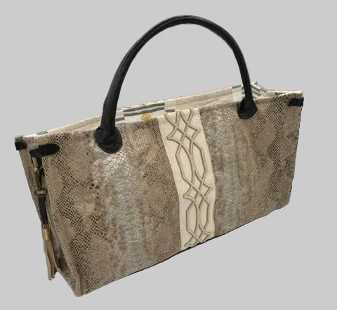 A rectangular tote bag with a snakeskin pattern in beige and brown, featuring a cream-colored geometric patterned band across the center and black leather handles, shown on a white circular backdrop.