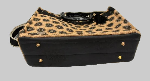 A leopard-print and black faux-leather handbag with gold-tone studs, displayed on a white surface between two black chairs.