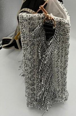 A close-up of a hand holding a woven handbag made from black and white tweed fabric with gold-tone hardware, set against a plain white background.
