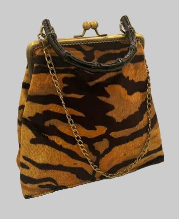 A small handbag with a tiger-stripe pattern in brown and black, featuring a gold-tone metal frame, kiss-lock closure, and chain strap, photographed on a plain light background.
